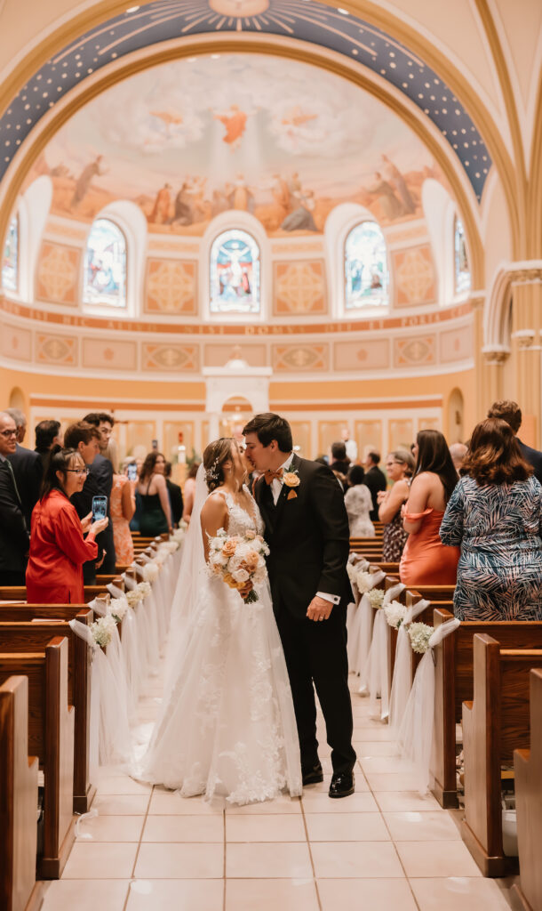 bride and groom kissing halfway down aisle, catholic church wedding, Michigan, Ann Arbor